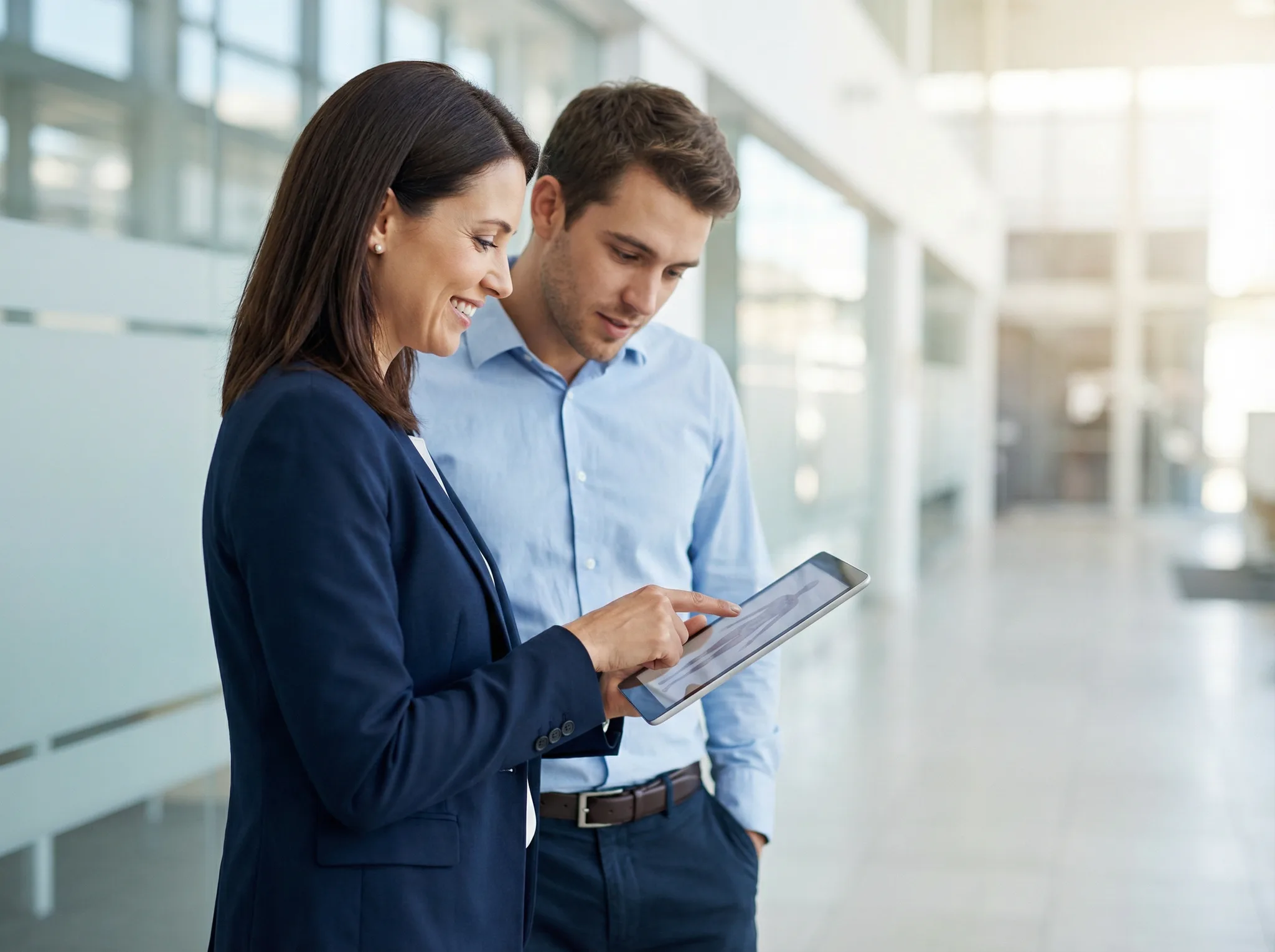 A woman points to a tablet while coaching a medical sales professional in a bright office